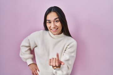 Young south asian woman standing over pink background beckoning come here gesture with hand inviting welcoming happy and smiling