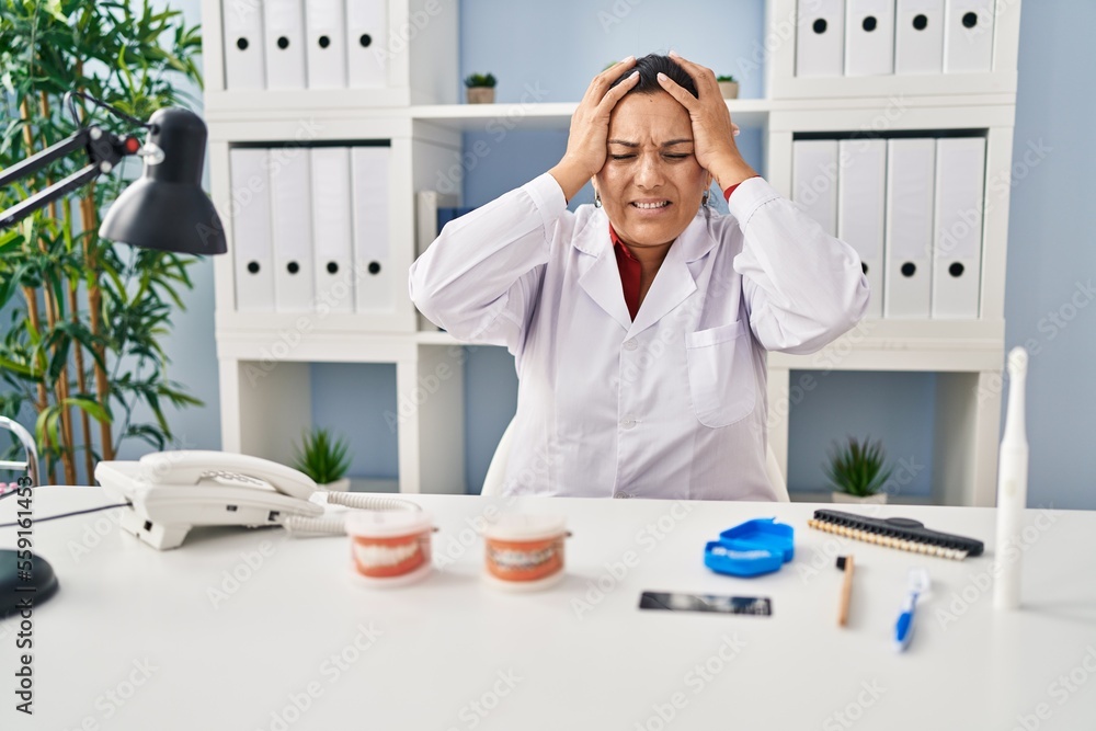 Poster hispanic mature dentist woman working at the clinic suffering from headache desperate and stressed b