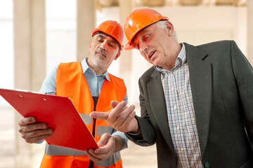 Construction supervisor, workers at a construction site. Managers wearing protective workwear, hard hat looking up pointing. Construction workforce, working labor man