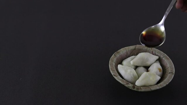 Nolen gur or date palm jaggery poured over puli pithe or bengali rice flour dumplings with coconut fillings served on a shal pata plate during poush sankranti or makar sankranti