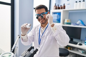 Young hispanic man scientist looking diamond by magnifying glasses at laboratory