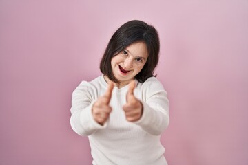 Woman with down syndrome standing over pink background pointing fingers to camera with happy and funny face. good energy and vibes.