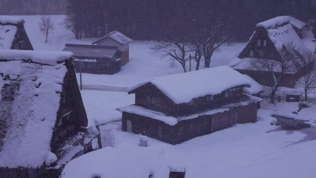 Snow falls on steep thatch roofs of Gokayama village in grey dawn