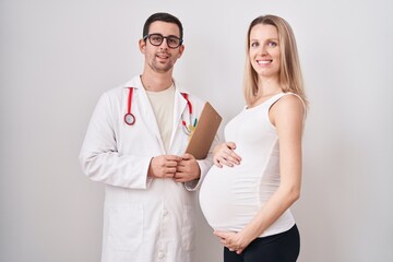 Young woman expecting a baby with doctor looking positive and happy standing and smiling with a...