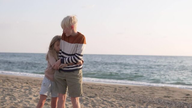 Cute children, brother and sister, hug each other against the backdrop of the sea.