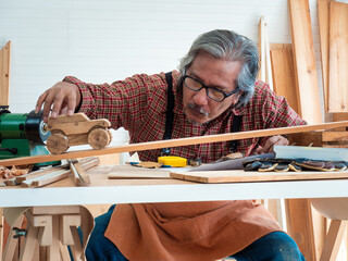 Happy Asian senior man is enjoying his hobby by diligently painting birdhouses in the workshop.