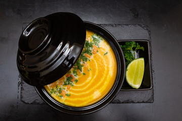 pumpkin soup in a black plate, on a black wooden background next to a slice of lemon