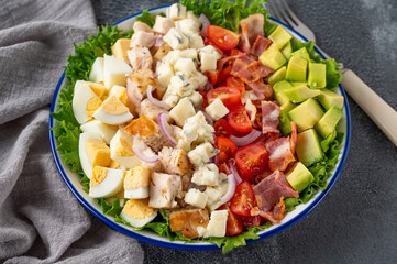 Tradition Cobb salad with fried chicken, avocado, fresh tomatoes, eggs, bacon and cheese on a plate on a dark background. Top view, copy space, selective focus