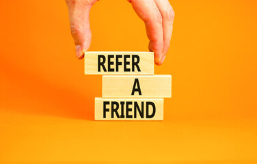 Refer a friend symbol. Concept words Refer a friend on wooden blocks on a beautiful orange table orange background. Businessman hand. Business and refer a friend concept. Copy space.