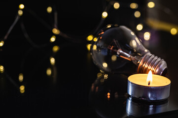 light bulbs and a burning candle on a black background.
also garland, bokeh. holiday blackout concept