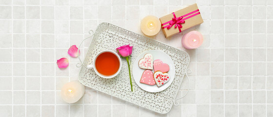Composition with tasty heart shaped cookies, cup of tea, gift and candles on light background. Valentine's Day celebration
