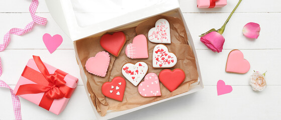 Box with tasty heart shaped cookies, gift and rose flowers on white wooden background. Valentine's...