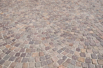 Fototapeta premium Cobblestone arched pavement road with red, brown, yellow and gray rocks. Tiled pavement background. Circle paving.