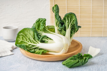 Wooden plate with fresh pak choi cabbage on light background