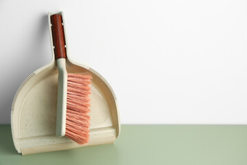 Dustpan and cleaning brush on color floor near light wall