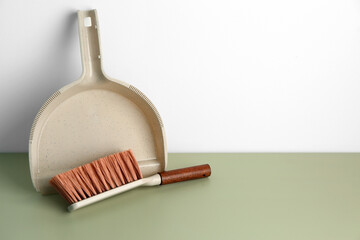 Dustpan and cleaning brush on color floor near light wall