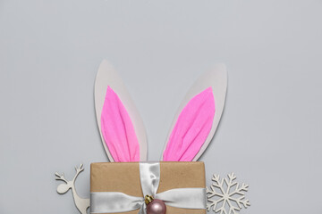 Paper bunny ears with gift and Christmas decor on grey background