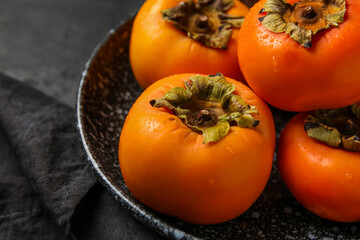 Plate with fresh ripe persimmons on dark background, closeup