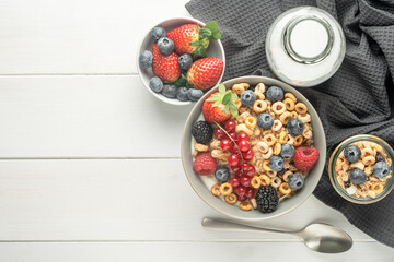 Cereal bowls with berries, spoon and a bottle of milk on a gray napkin on a white table. Healthy eating concept. Front view
