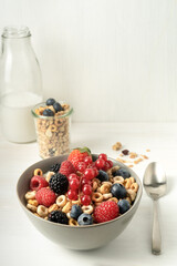 Cereal bowls with berries, spoon and a bottle of milk on a white table. Healthy eating concept. Front view.