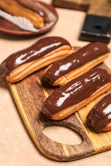 Wooden board with tasty chocolate eclairs on color background, closeup