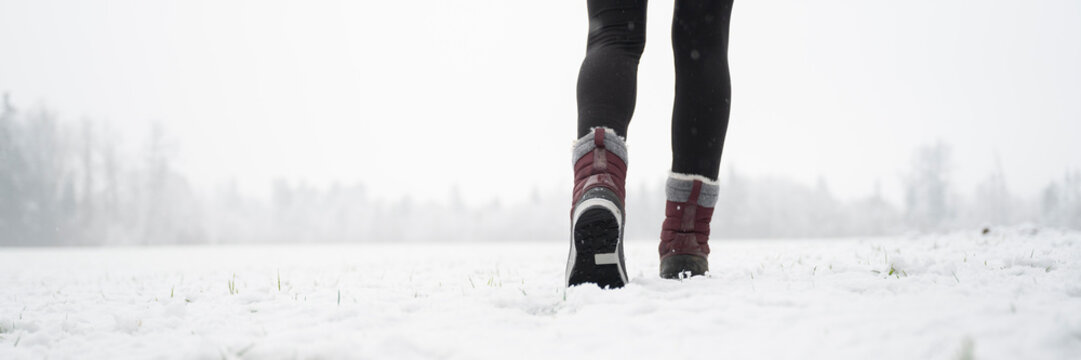 Female legs in winter boots walking in snow covered nature
