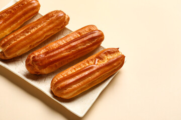 Plate with sweet eclairs on color background