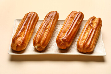 Plate with sweet eclairs on color background