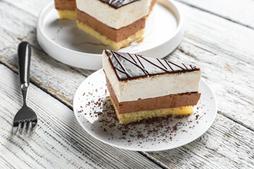 Plates with pieces of birds milk cake and fork on white wooden background