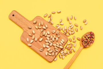 Cutting board and wooden spoon with tasty pistachio nuts on yellow background