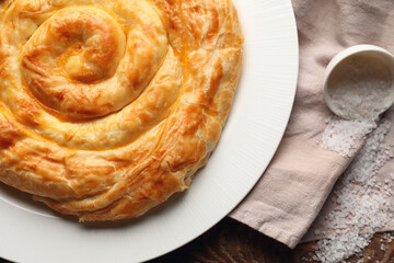 Plate with delicious cheese pie and overturned bowl of salt on napkin, closeup