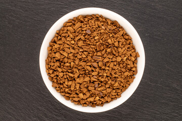 Fragrant instant coffee in a white saucer on slate stone, macro, top view.