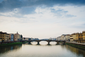 Fototapeta premium Panoramic view of the Ponto Vecchio Bridge and the Arno River in Florence. Reflection in the water of buildings and roofs of houses. Fog, Perspective, typical Tuscan landscape