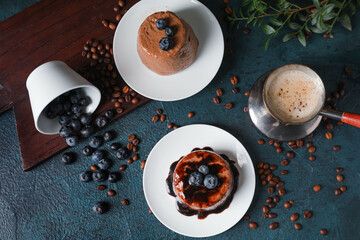 Plates with delicious chocolate pudding, overturned cup of blueberry, coffee beans and cappuccino...