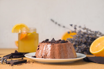 Plate with delicious pudding, chocolate and lemonade on beige table near grey wall