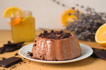 Plate with delicious pudding, chocolate and lemonade on beige table near grey wall