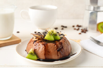 Plate with delicious pudding, chocolate sauce, kiwi and coconut slices on white table