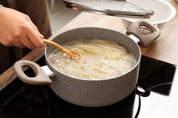 Woman preparing delicious pasta on electric stove in kitchen