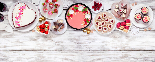 Valentines Day top border with a variety of desserts and sweets. Overhead view on a white wood banner background. Love and hearts theme. Copy space.