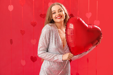 Beautiful young woman with heart-shaped balloon on red background. Valentine's Day celebration