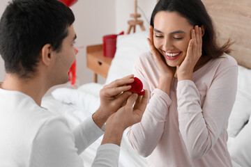 Young man proposing to his beloved girlfriend in bedroom on Valentine's Day