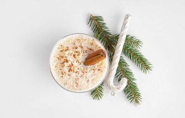 Glass of tasty eggnog cocktail, fir branch and Christmas decoration on white background