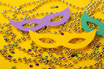 Mardi Gras gold color beads with Masquerade festival carnival masks and golden, green, purple confetti on yellow background.