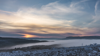 Winter panorama at sunset with snow covered hills with low fog in the valley and cloud cover, hills with snow and trees in winter at sunset © Denis