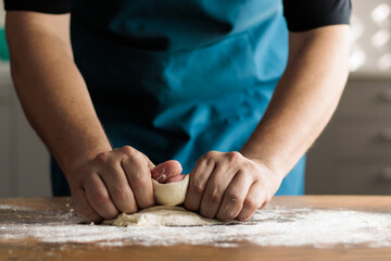 Unrecognizable man kneading by hand on a wooden table in the kitchen of his home