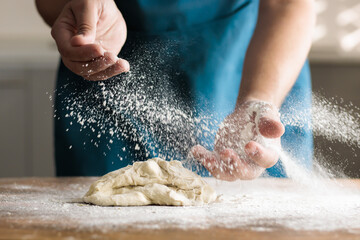 Unrecognisable man kneading by hand in kitchen, on wooden table. Spreading flour