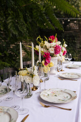 Flowers decorations on the table. Beautiful plates and candles.  Table setting by the pink, yellow. white flowers outdoor.