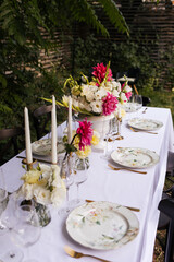 Flowers decorations on the table. Beautiful plates and candles.  Table setting by the pink, yellow. white flowers outdoor.