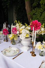 Flowers decorations on the table. Beautiful plates and candles.  Table setting by the pink, yellow. white flowers outdoor.