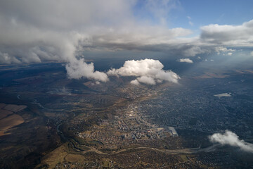 Aerial view from airplane window at high altitude of distant city covered with white puffy cumulus...